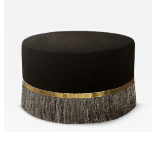 Black ottoman with brass fringe detail, rounded shape.